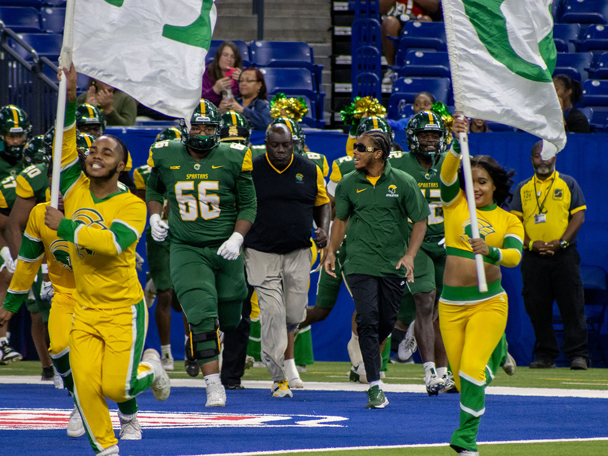 two people with flags and a football team running out behind them